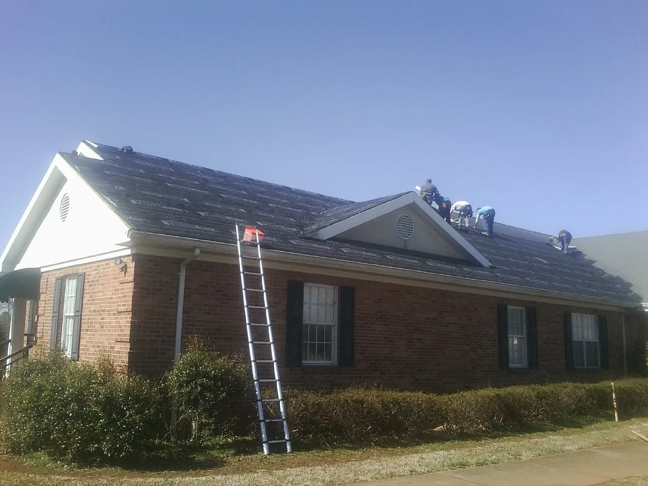 Crew tearing shingles off a brick ranch roof with a ladder set — Emergency Roof Repair work by our crew in Slater