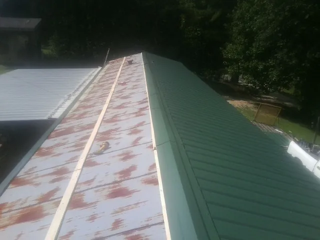 Old rusted panels beside newly installed green metal roofing — Wind Damage Roof Repair by Roofing Brothers in Slater