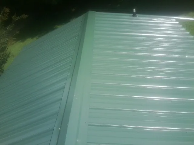 New green metal panels meeting at the ridge of a roof — Flat Roof Repair work by our crew in Slater