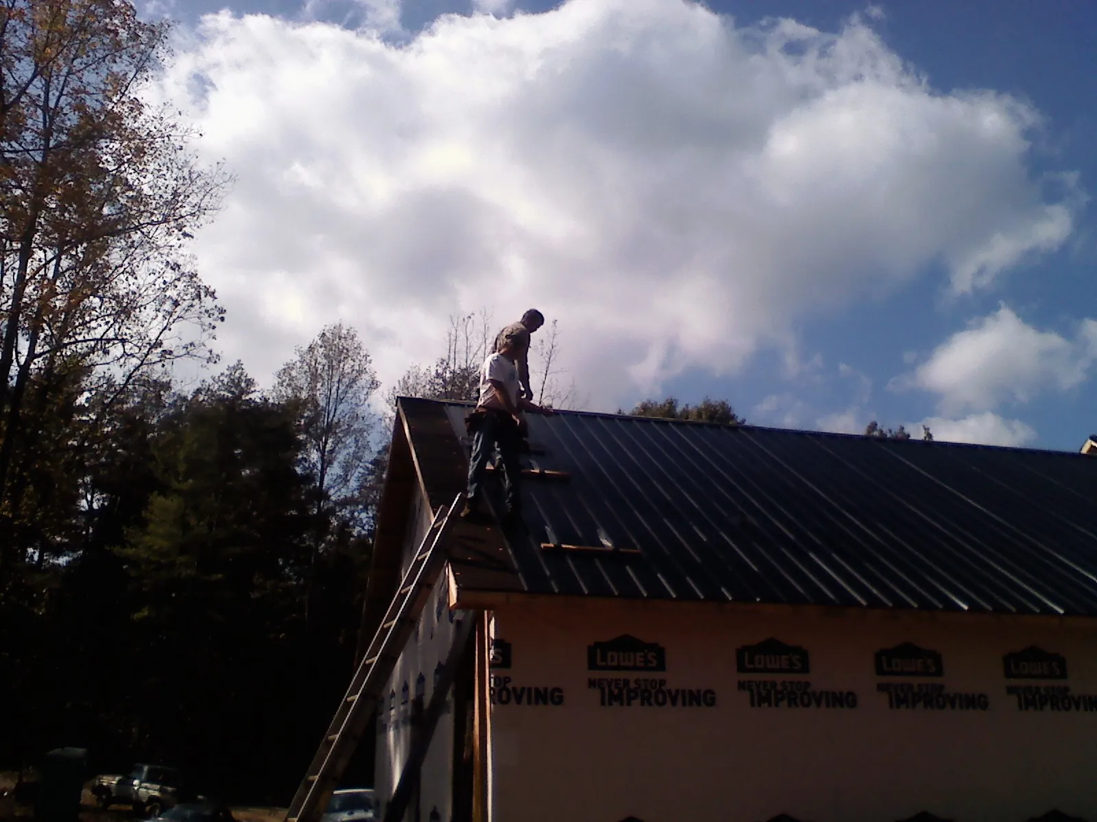 Roofer fastening dark metal panels high against a cloudy sky, from a Roof Inspection job in Slater