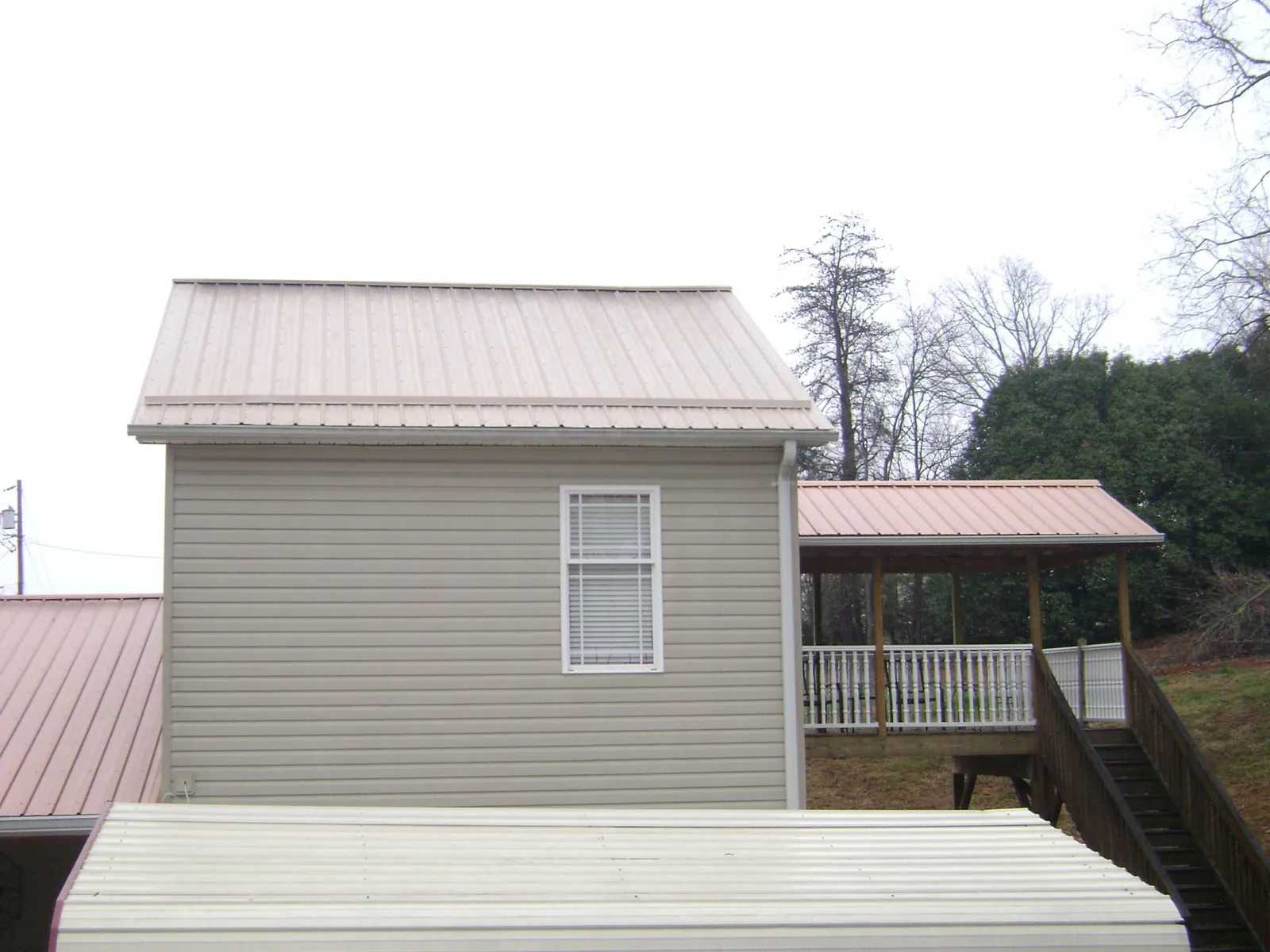 Tan metal roofs on a two story addition and attached porch, from a Roof Replacement job in Slater